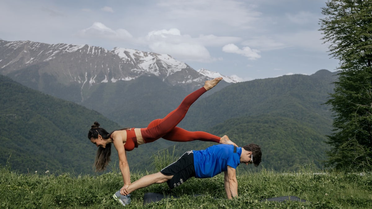 Couple doing yoga exercises outdoors with a breathtaking mountain view.