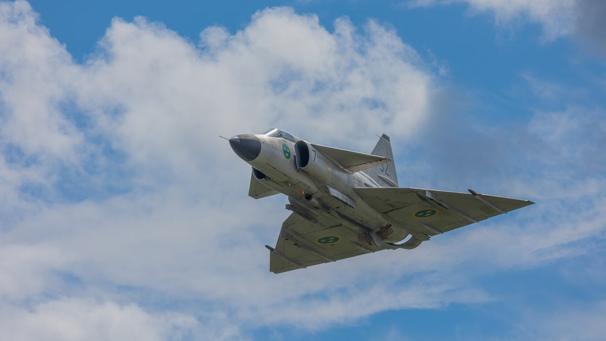 A majestic fighter jet flying through a clear blue sky, demonstrating speed and power against fluffy white clouds.